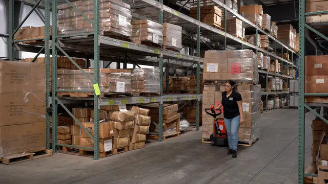 Warehouse worker using an electric pallet jack to move goods.