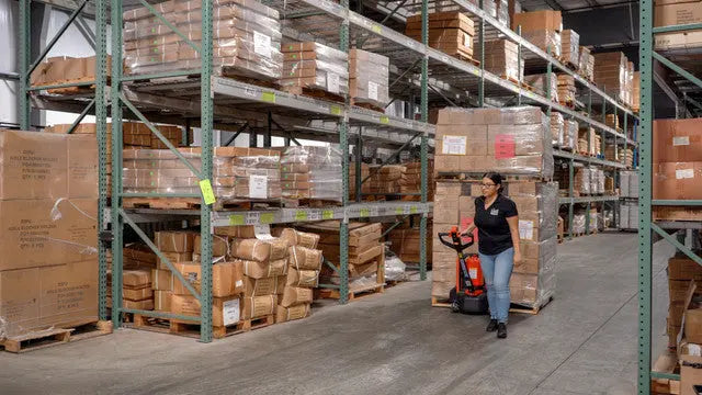 Warehouse worker using an electric pallet jack to move goods.