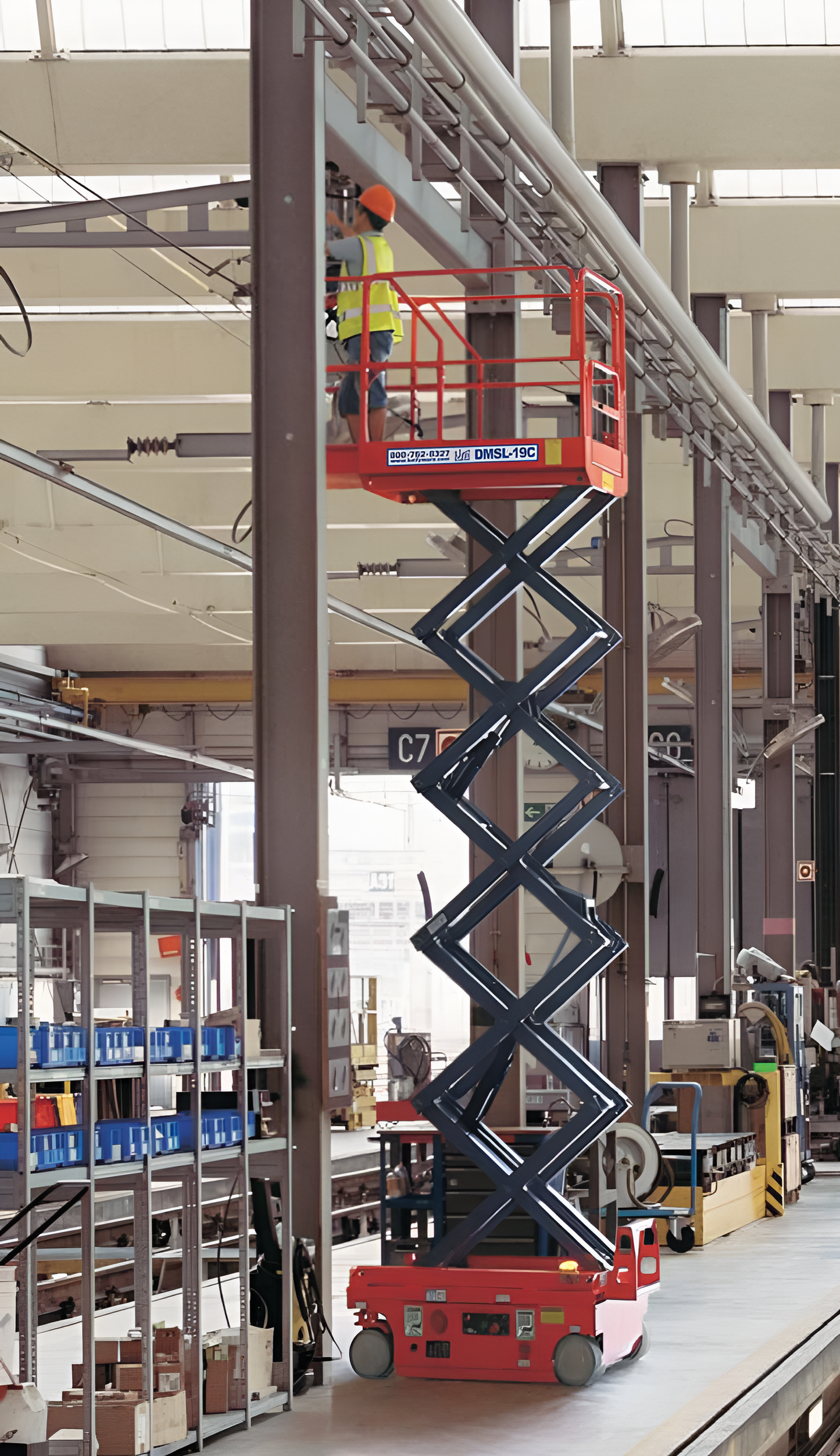 Worker using an orange scissor lift for overhead tasks in a warehouse.