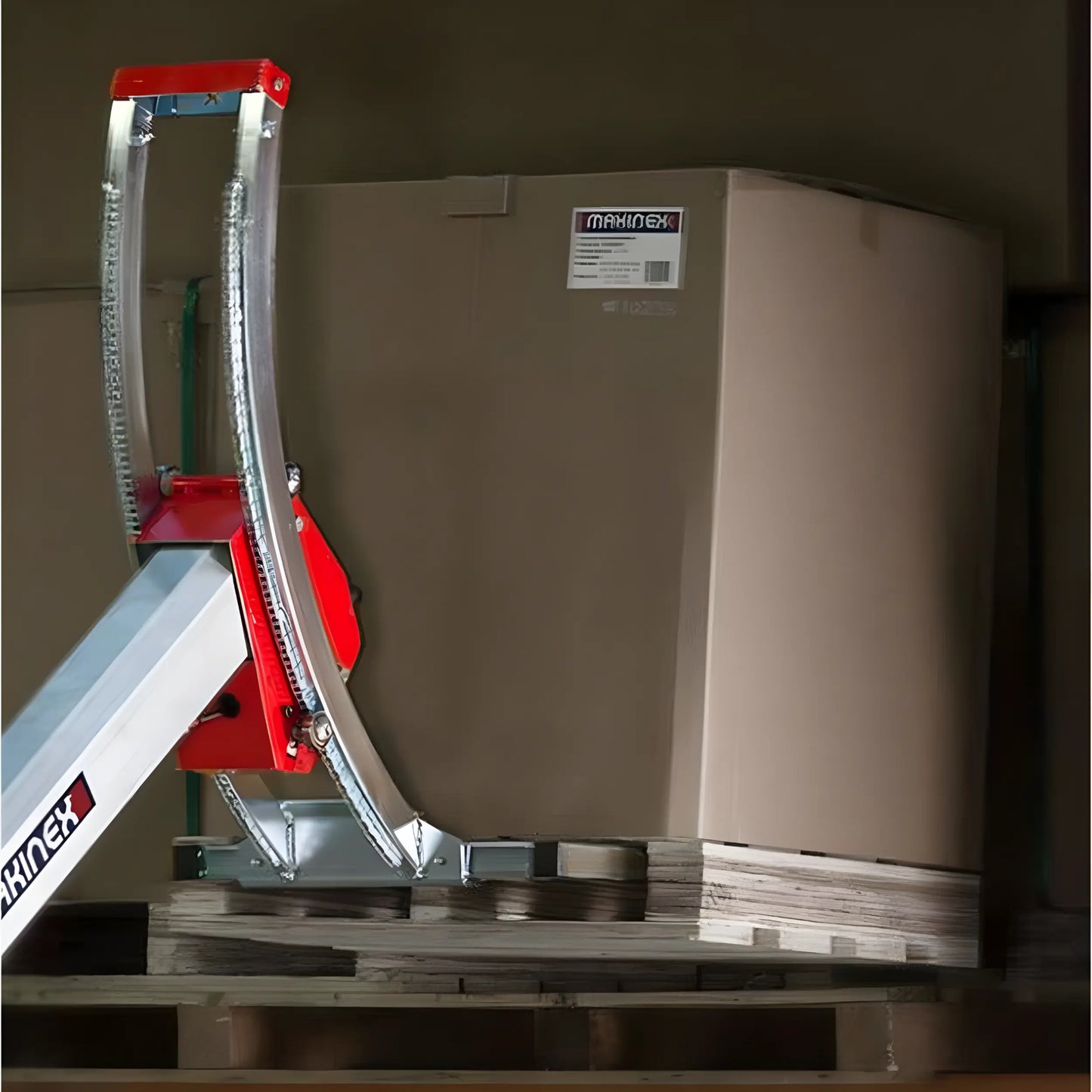 Red lifting device handling a large cardboard box on a pallet.