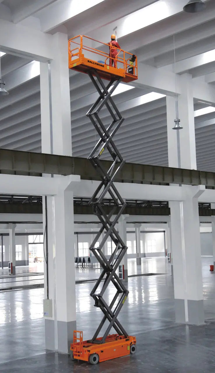 Ballymore drivable scissor lift in warehouse with worker operating elevated platform in orange