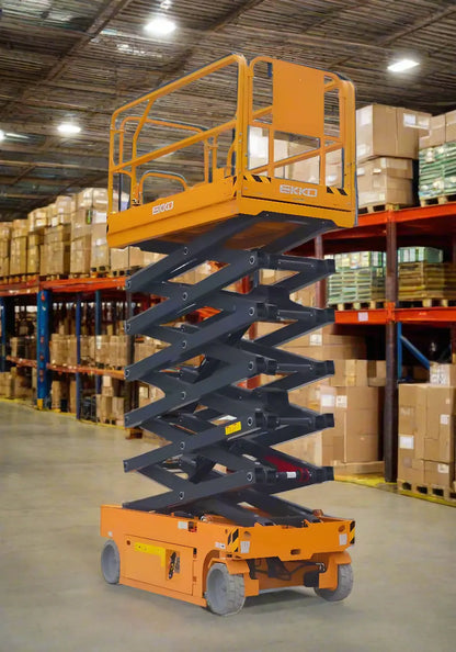 Orange EKKO ES100E scissor lift elevated inside warehouse with boxes on shelves