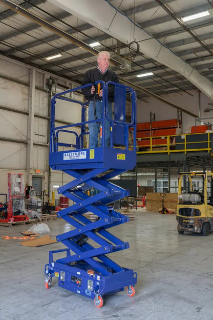 Ballymore compact scissor lift in blue with operator elevated inside industrial warehouse